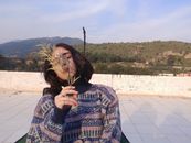 Woman sitting outdoors covering face with leaves, in Aydın, Turkey.